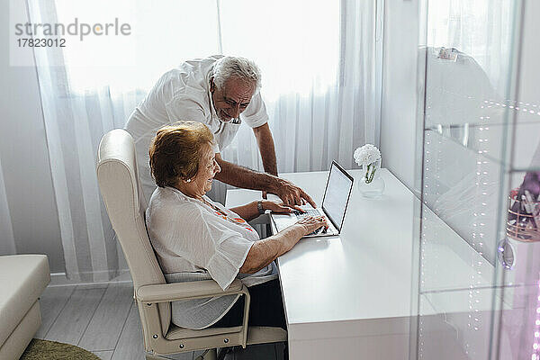 Lächelnder Mann erklärt der älteren Mutter zu Hause den Laptop