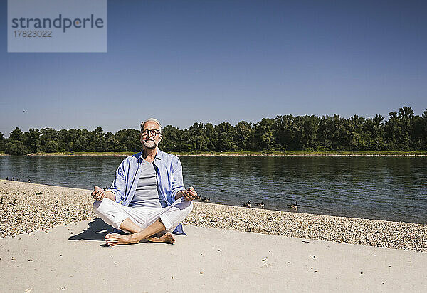 Lächelnder Mann meditiert am Flussufer