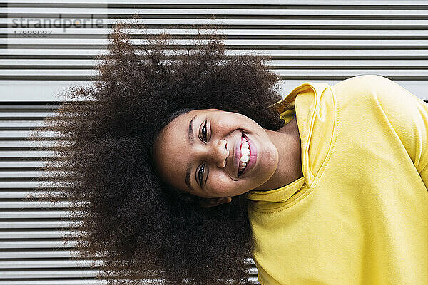 Happy girl with Afro hairstyle standing in front of wall