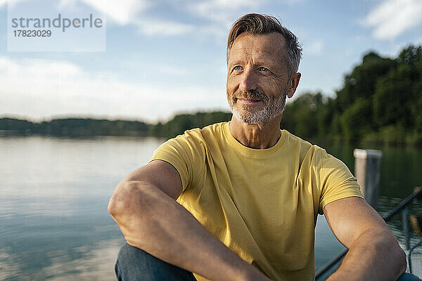 Nachdenklicher reifer Mann sitzt an einem sonnigen Tag am See