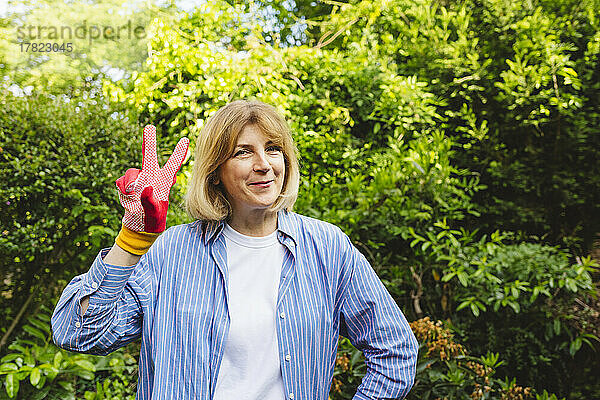 Lächelnde Frau zeigt im Garten ein Siegeszeichen