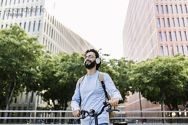 Glücklicher Mann mit kabellosen Kopfhörern  der mit dem Fahrrad steht