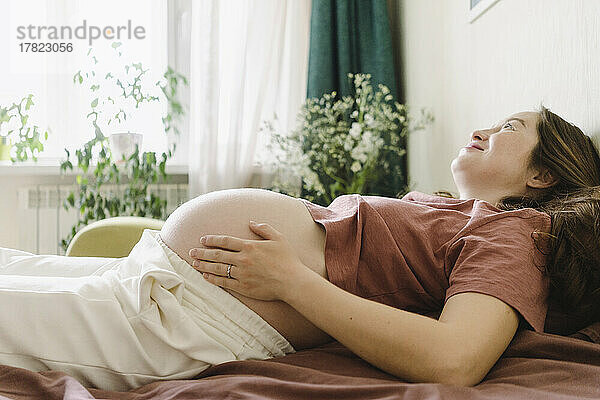 Lächelnde schwangere Frau  die zu Hause auf dem Schlafsofa liegt