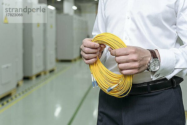 Geschäftsmann hält gerollte gelbe Kabel in der Fabrik
