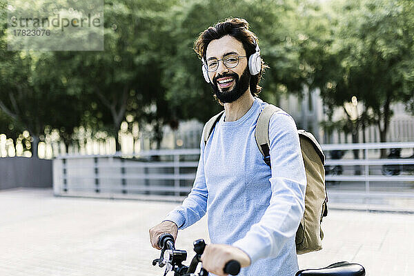 Lächelnder Mann mit kabellosen Kopfhörern  der mit dem Fahrrad steht