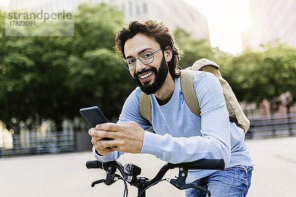 Glücklicher Mann benutzt Smartphone und stützt sich auf Fahrrad
