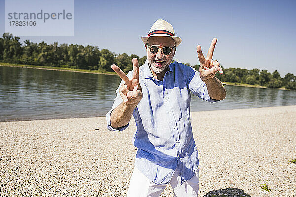 Glücklicher älterer Mann gestikuliert an einem sonnigen Tag am Flussufer