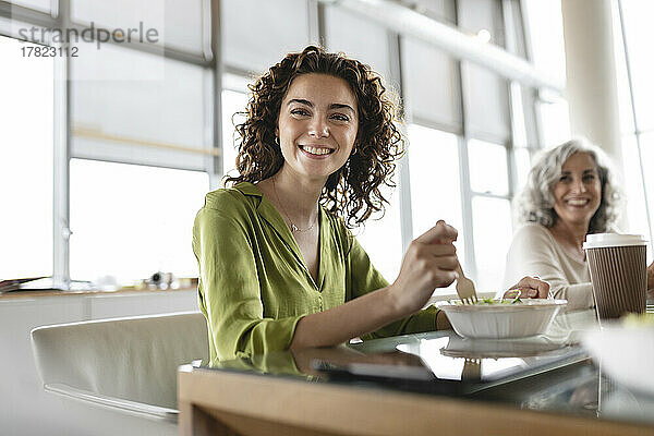 Glückliche junge Geschäftsfrau mit einer Schüssel Salat am Schreibtisch