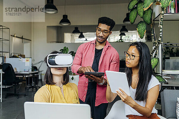 Geschäftsfrau mit VR-Brille von Kollegen mit Tablet-PCs am Arbeitsplatz