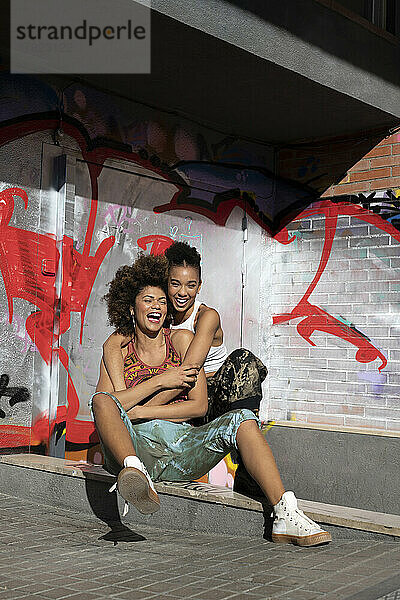 Glückliche Freunde  die sich an einem sonnigen Tag vor der Graffitiwand umarmen