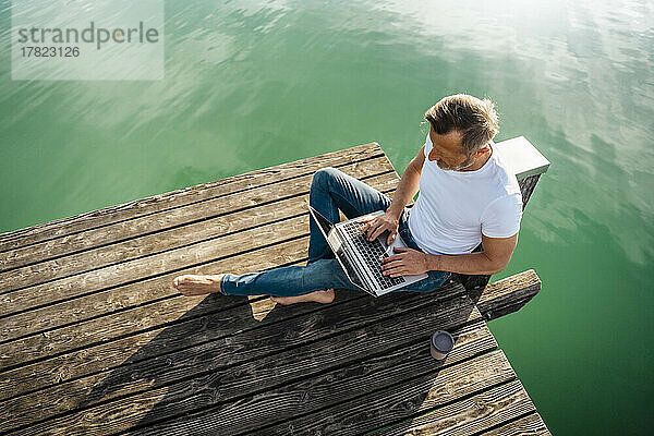 Freiberufler arbeitet am Laptop und sitzt am Pier über dem See
