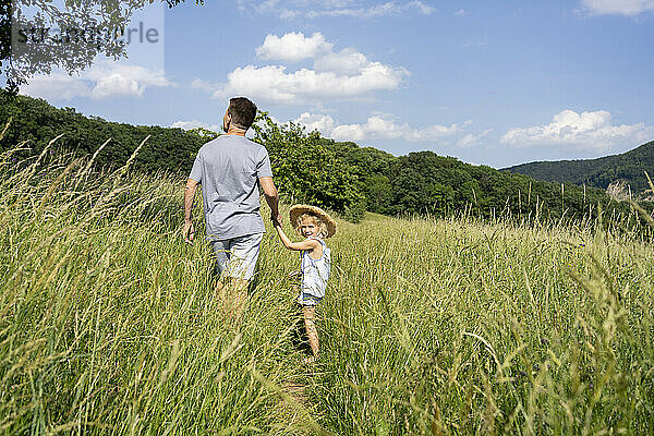 Vater und Tochter gehen an einem sonnigen Tag durch das Feld
