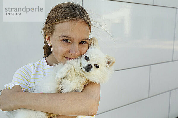 Glückliches Mädchen umarmt Hund vor der Wand