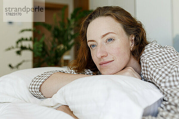 Thoughtful woman lying on bed with pillow in bedroom