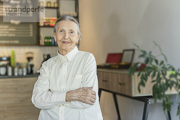 Lächelnde ältere Frau mit verschränkten Armen steht im Café