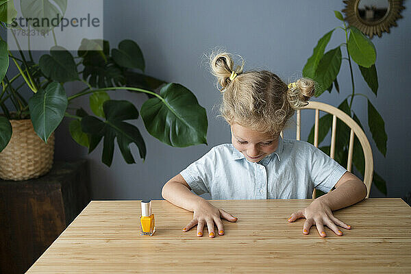 Lächelndes Mädchen  das lackierte Nägel auf dem Tisch betrachtet
