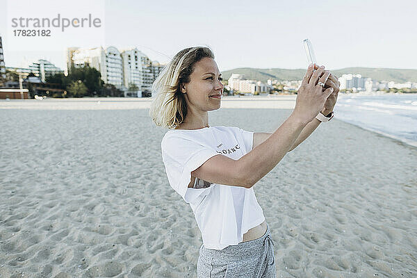 Lächelnde Frau  die am Strand ein Selfie mit ihrem Smartphone macht