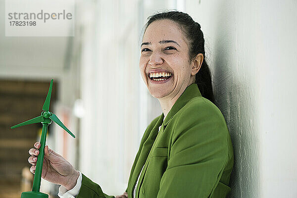 Fröhliche Geschäftsfrau mit Windturbinenmodell an der Wand