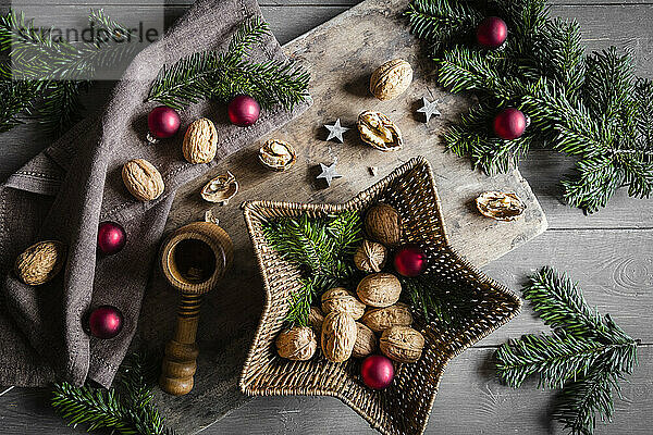 Studioaufnahme von Schneidebrett  sternförmigem Weidenkorb  Zweigen  Weihnachtsschmuck  Walnüssen und einfachem Nussknacker