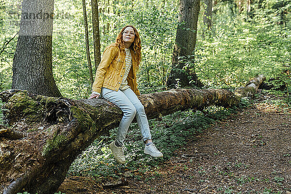 Young woman sitting on fallen tree trunk in forest