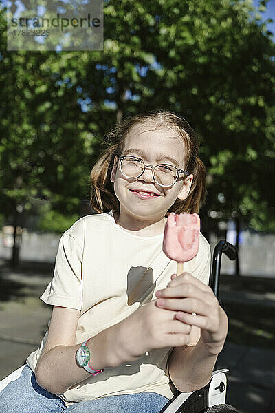 Lächelndes Mädchen sitzt mit Eis im Rollstuhl im Park