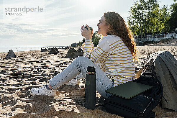 Lächelnde Frau trinkt Kaffee in einer isolierten Tasse am Strand