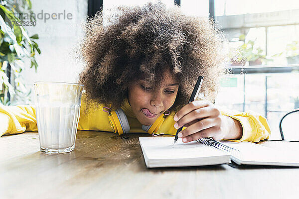 Mädchen mit Afro-Frisur schreibt in Notizbuch und sitzt im Café