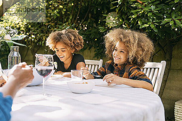 Lächelnder Junge und Schwester essen am Esstisch im Hinterhof zu Mittag