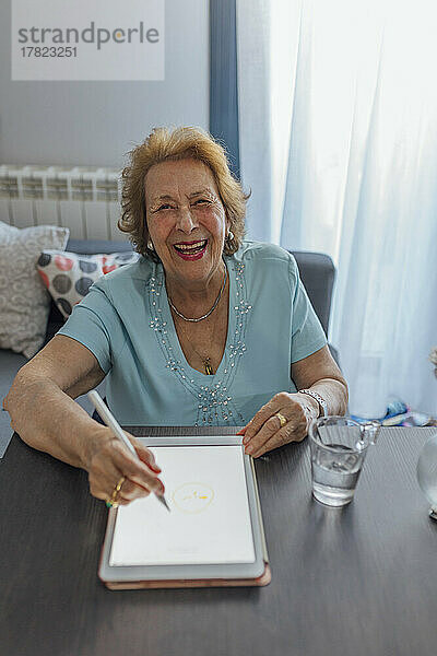 Fröhliche ältere Frau mit Tablet-PC sitzt am Tisch