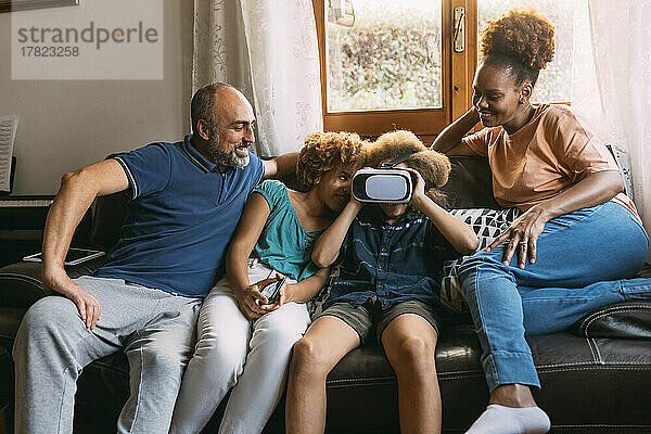 Junge mit Virtual-Reality-Simulator sitzt neben Schwester und Eltern auf dem Sofa