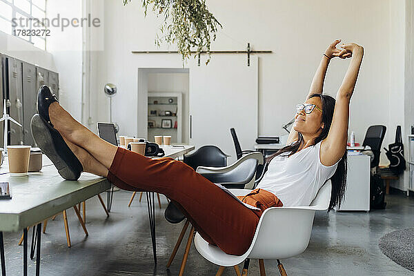 Smiling businesswoman stretching arms on chair at workplace