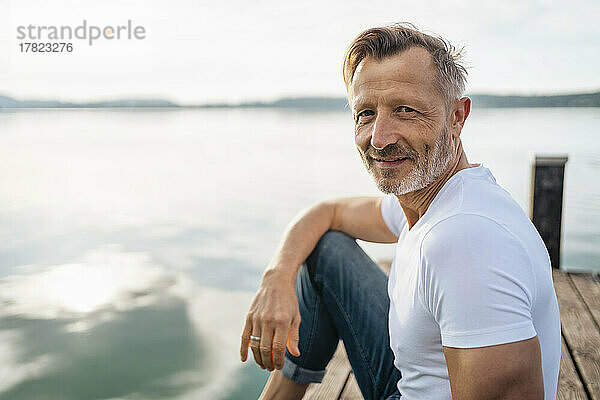 Lächelnder Mann sitzt auf der Anlegestelle am See