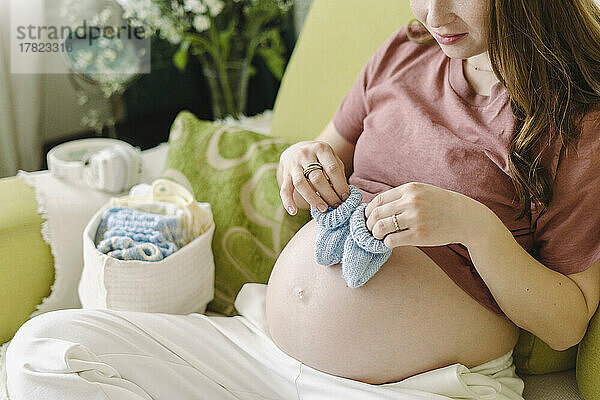 Schwangere Frau hält zu Hause gehäkelte Babyschuhe auf dem Bauch