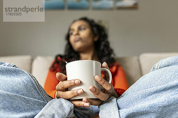 Nachdenkliche Frau mit Kaffeetasse sitzt im Wohnzimmer