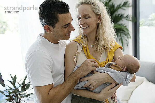 Lächelnde Frau mit Baby im Arm sitzt neben Mann zu Hause