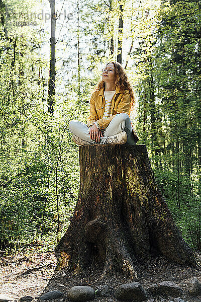 Young woman with eyes closed sitting on tree stump in forest