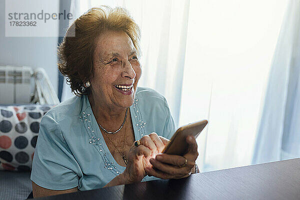 Glückliche ältere Frau mit Smartphone sitzt zu Hause