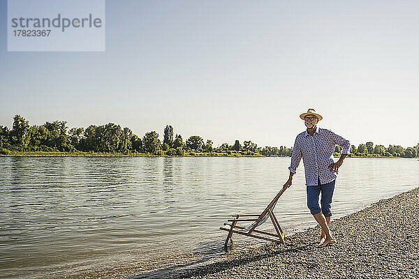 Mann mit Hut steht mit der Hand auf der Hüfte am Flussufer