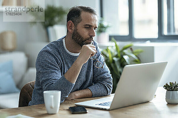 Nachdenklicher Geschäftsmann mit Brille und Blick auf den Laptop  der von zu Hause aus arbeitet