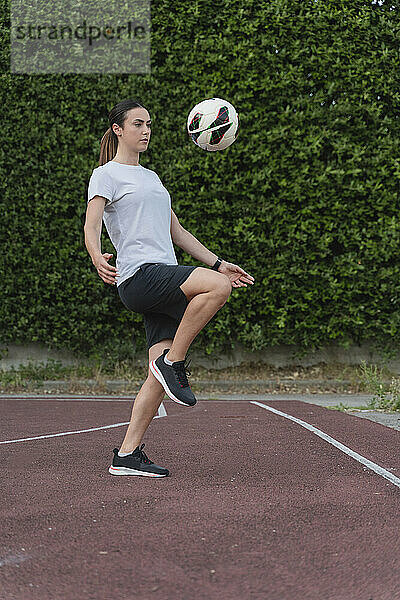 Junge Frau tritt Fußball mit Knie auf Sportplatz