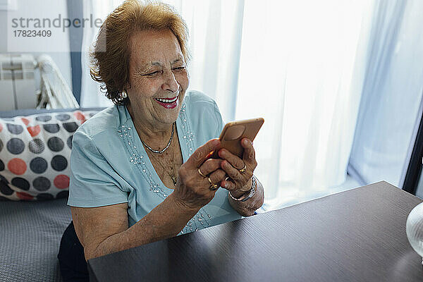 Happy senior woman using smart phone sitting at home