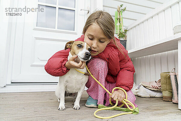 Mädchen mit Haustierleine streichelt Hund auf der Veranda
