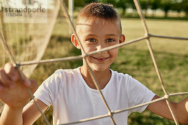 Lächelnder Junge  der an einem sonnigen Tag durch das Netz gesehen wird