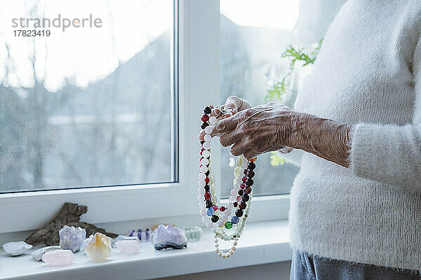 Hände einer älteren Frau mit einer Halskette aus Edelsteinperlen
