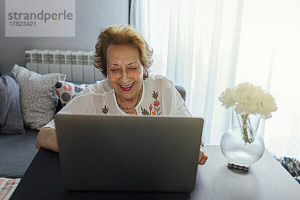 Lächelnde ältere Frau  die zu Hause einen Laptop benutzt