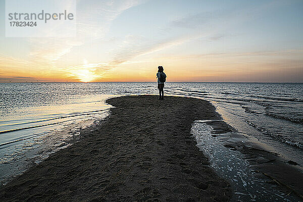 Frau steht bei Sonnenuntergang an der Küste