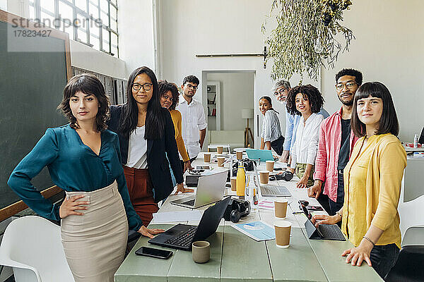 Selbstbewusste  gemischtrassige Kollegen stehen am Schreibtisch im Coworking-Büro