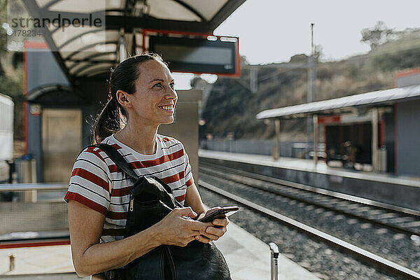 Lächelnde Frau mit Smartphone steht am Bahnhof