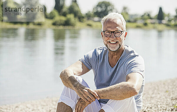 Lächelnder älterer Mann mit Brille sitzt am Flussufer