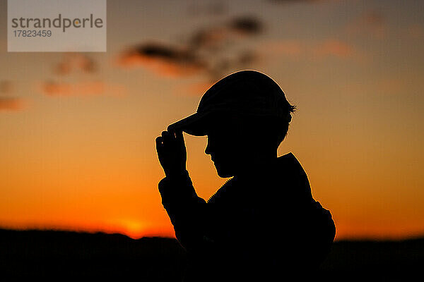 Silhouette eines Jungen mit Mütze bei Sonnenuntergang